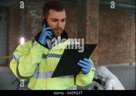 Man holding notepad and talking by phone. Two detectives are collecting evidence in a crime scene. Stock Photo
