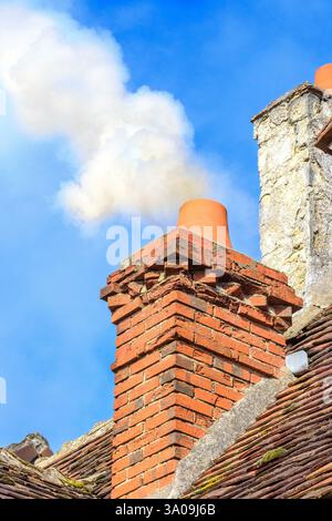 Brick house chimney belching a lot of polluting smoke from log fire - France. Stock Photo
