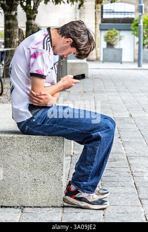 Young male sitting on stone block studying smartphone - Tours, Indre-et-Loire (37), France. Stock Photo