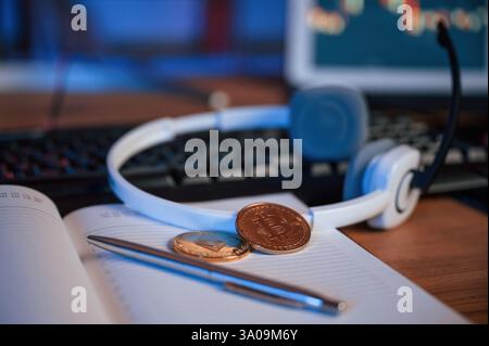 Close up view of physical bitcoins, headphones, notepad and pen that is on the table. Stock Photo