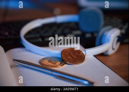 Close up view of physical bitcoins, headphones, notepad and pen that is on the table. Stock Photo