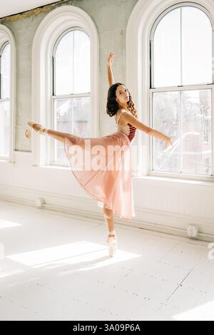 Ballerina performs an arabesque en pointe in a sunlit studio Stock Photo