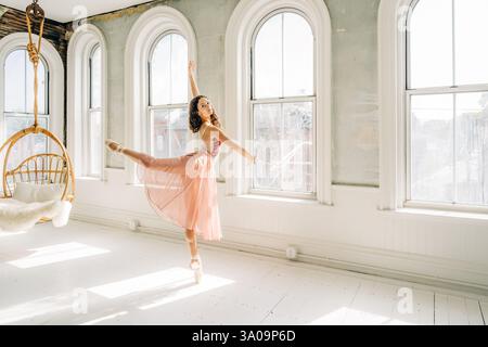 Ballerina performs an arabesque en pointe in a sunlit vintage studio Stock Photo