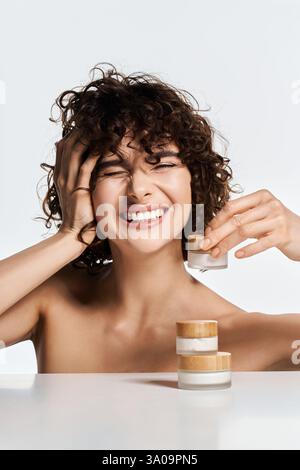 Joyful young woman smiles while holding a skincare jar, embodying beauty and confidence. Stock Photo
