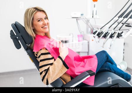 Happy young woman at dental clinic. Professional dental care and hygiene. She is showing thumbs up. Stock Photo