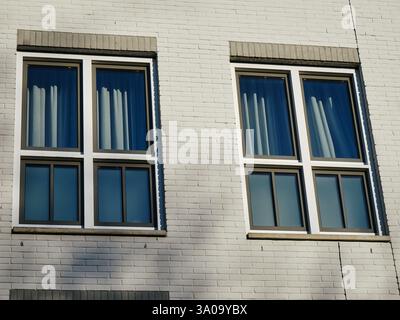 A close-up view of a modern residential facade featuring two large, double-paned windows with dark frames. The white brick exterior is complemented by Stock Photo