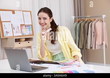 Fashion designer with sketches of clothes and color palettes working at white table in workshop Stock Photo