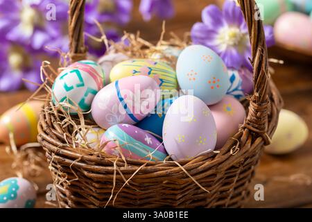 Decorated Easter eggs in a basket with purple daisies on  a wooden table Stock Photo