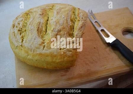 A loaf of freshly baked bread with a golden brown, crispy crust and a soft, fluffy interior, sliced open on a wooden cutting board with a bread knife Stock Photo