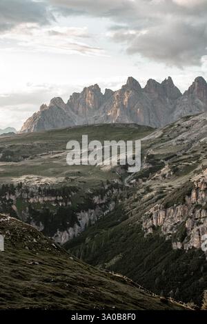 Majestic mountain range rises dramatically in the background, displaying rugged peaks under a cloudy sky. Lush green valleys stretch below, highlighti Stock Photo