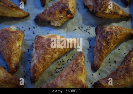 A baking tray filled with freshly baked golden brown triangular cakes. The cakes have a flaky, crunchy texture, are sprinkled with sezam seeds on top. Stock Photo