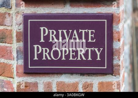 A purple private property sign  with yellow writing on a brick wall. Stock Photo