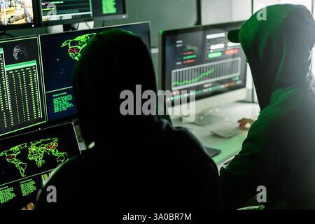 Hackers working on computers showing world maps and security camera footage Stock Photo