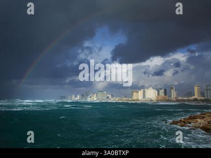 Stormy sea with dark clouds and a rainbow over Tel Aviv's skyline Stock Photo