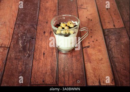A glass of dessert with nuts on top. The dessert is in a clear glass and is sitting on a wooden table Stock Photo
