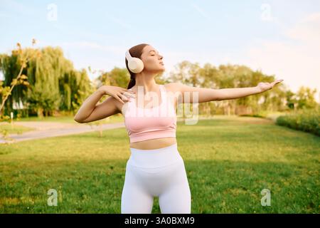 A young athlete embraces the joy of exercise while wearing headphones and dancing outdoors. Stock Photo