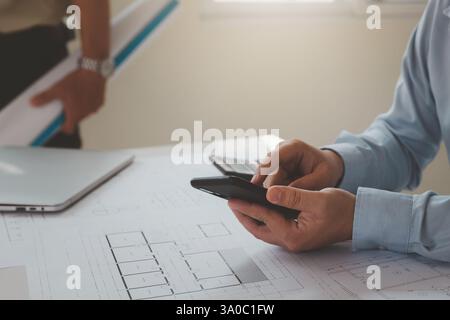Engineer or Architect using smartphone on blueprint in his home office.  Concept Work from home. Stock Photo