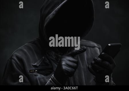Hooded computer hacker using smartphone, selective focus Stock Photo