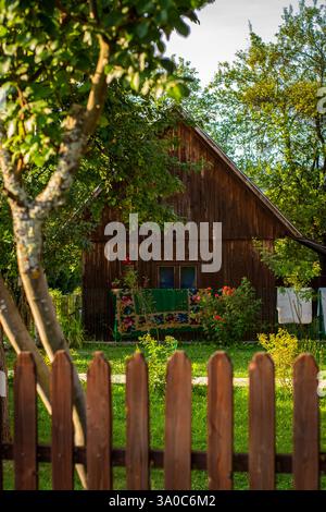 Old idyllic house in the nature with a wooden fence and a traditional folk pattern carpet hanging outside Stock Photo