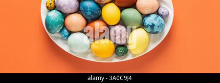 Top view of oval dish with dyed natural dyes Easter eggs on orange background, Happy Easter Stock Photo