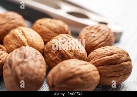 Whole walnuts with a nutcracker. Close-up of textured brown shells. Healthy snack rich in nutrients and omega-3. Selective focus. Stock Photo