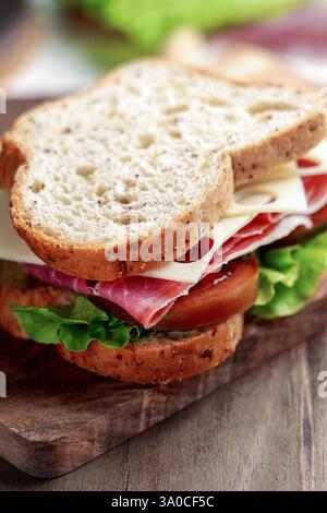 Whole grain bread sandwich with cured ham, Kumato tomato, Swiss cheese and fresh lettuce on a wooden board Stock Photo
