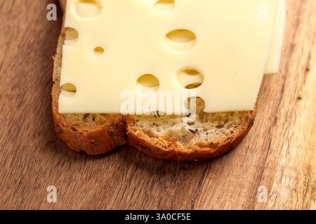 Fresh sandwich with slice of Emmental on whole grain bread. Round holes of soft yellow cheese and crispy toast. Rustic wooden surface. Close up. Stock Photo