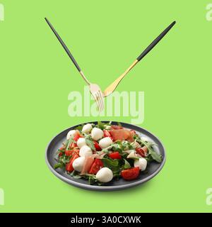 Cutlery in air over plate with tasty salad on light green background Stock Photo