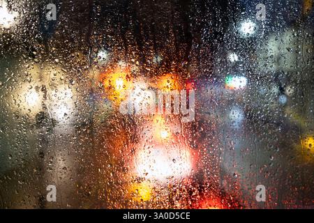 View of colourful shop and car traffic lights on a street at night in London view through a double decker bus top floor rainy window London UK Stock Photo