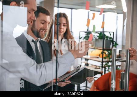 Group of coworkers in the office is standing together and putting stickers on the glass. Stock Photo