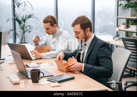 Two coworkers are eating food that is in the eco boxes. Sitting in the office. Stock Photo