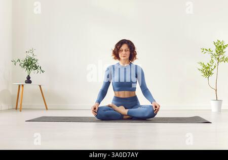 Yogi sporty attractive woman practicing yoga, doing Ardha Padmasana exercise, meditating in Half Lotus  Stock Photo