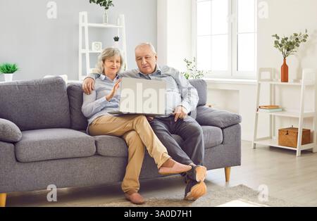 Senior couple having video call sitting on sofa at home. Retirement and technology concept. Stock Photo