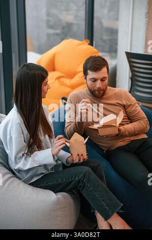 Sitting and talking. Office workers are in the rest zone is having a break and eating food from paper eco boxes. Stock Photo