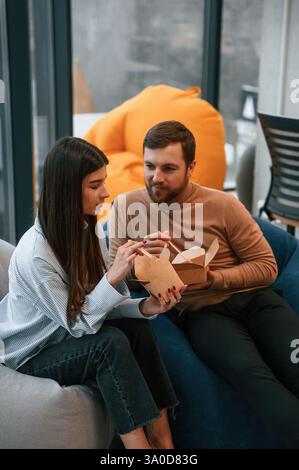 Sitting and talking. Office workers are in the rest zone is having a break and eating food from paper eco boxes. Stock Photo