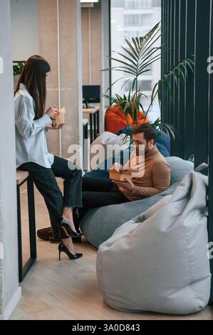 Office workers are in the rest zone is having a break and eating food from paper eco boxes. Stock Photo