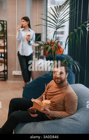 Office workers are in the rest zone is having a break and eating food from paper eco boxes. Stock Photo