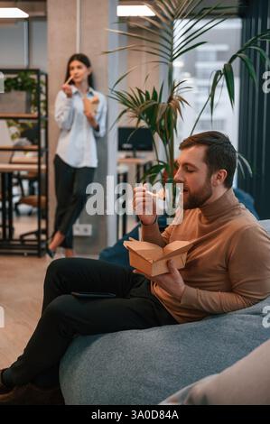 Office workers are in the rest zone is having a break and eating food from paper eco boxes. Stock Photo