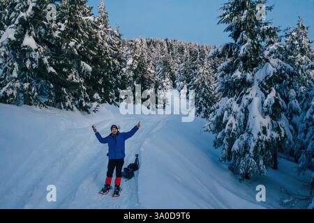 Man in snowshoes is standing, holding drone controller. In the majestic forest of Carpathian mountains. Stock Photo