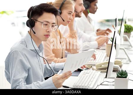 Asian hotline operator working with documents, providing technical support services to clients, free space Stock Photo