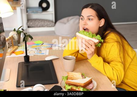 Young woman eating tasty sandwich in office Stock Photo