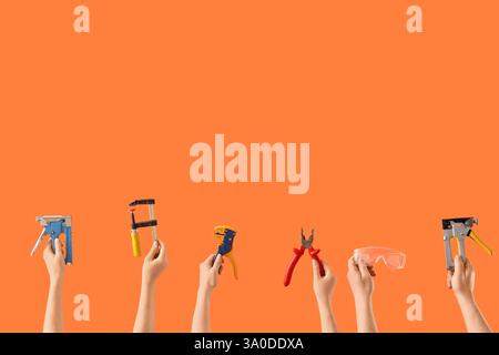 Many hands with construction tools on orange background Stock Photo