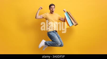 Overjoyed man jumping with shopping bags against yellow background Stock Photo