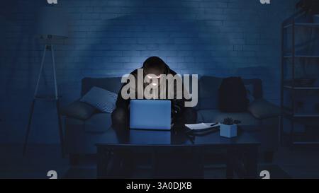 Masked hacker downloading private information using laptop Stock Photo