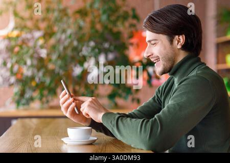 Young man using smartphone while drinking coffee at cafe Stock Photo