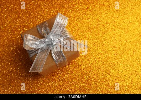 Gift box with silver glitter ribbon bow on a gold background Stock Photo
