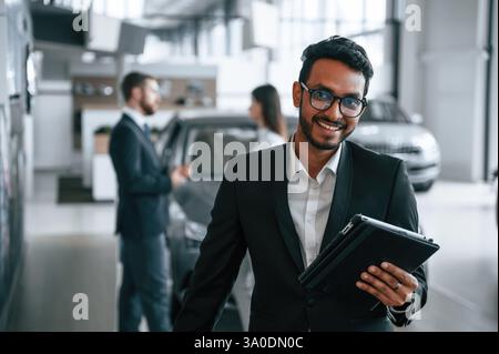 Using graphic tablet. Three people are working together in the car showroom. Stock Photo