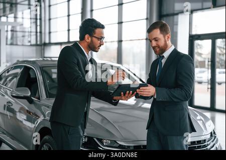 Using graphic tablet. Man is consulting the customer in the car showroom. Stock Photo