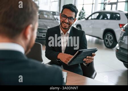 Using graphic tablet. Man is consulting the customer in the car showroom. Stock Photo