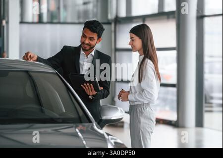 Man in formal clothes is consulting woman about the automobile in the car dealership. Stock Photo